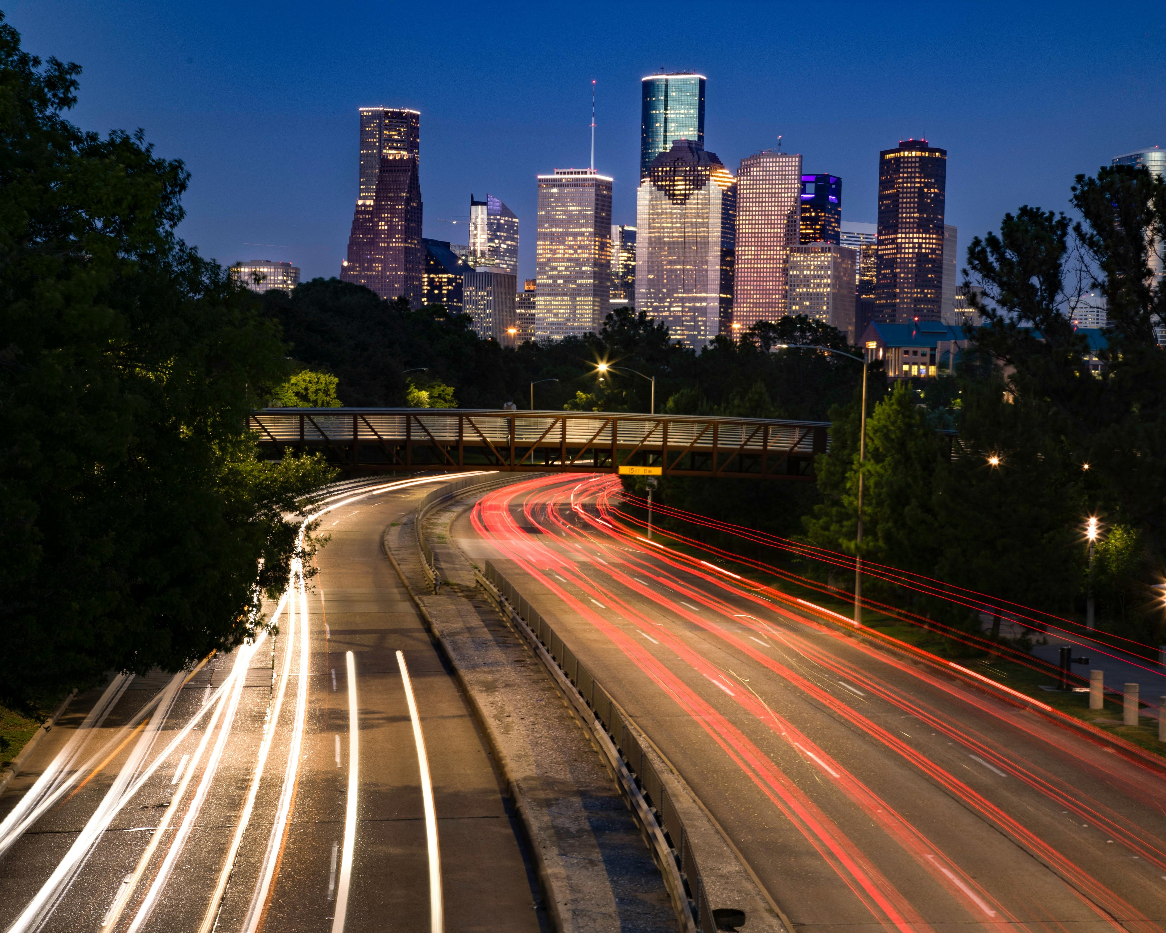 Houston skyline in background with traffic light blurs on highway in foreground. Photo by Trace Hudson: https://www.pexels.com/photo/an-aerial-photography-of-city-buildings-at-night-near-the-road-7142456/