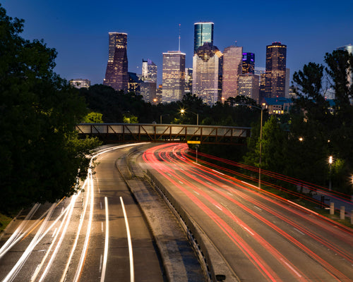 Houston skyline in background with traffic light blurs on highway in foreground. Photo by Trace Hudson: https://www.pexels.com/photo/an-aerial-photography-of-city-buildings-at-night-near-the-road-7142456/