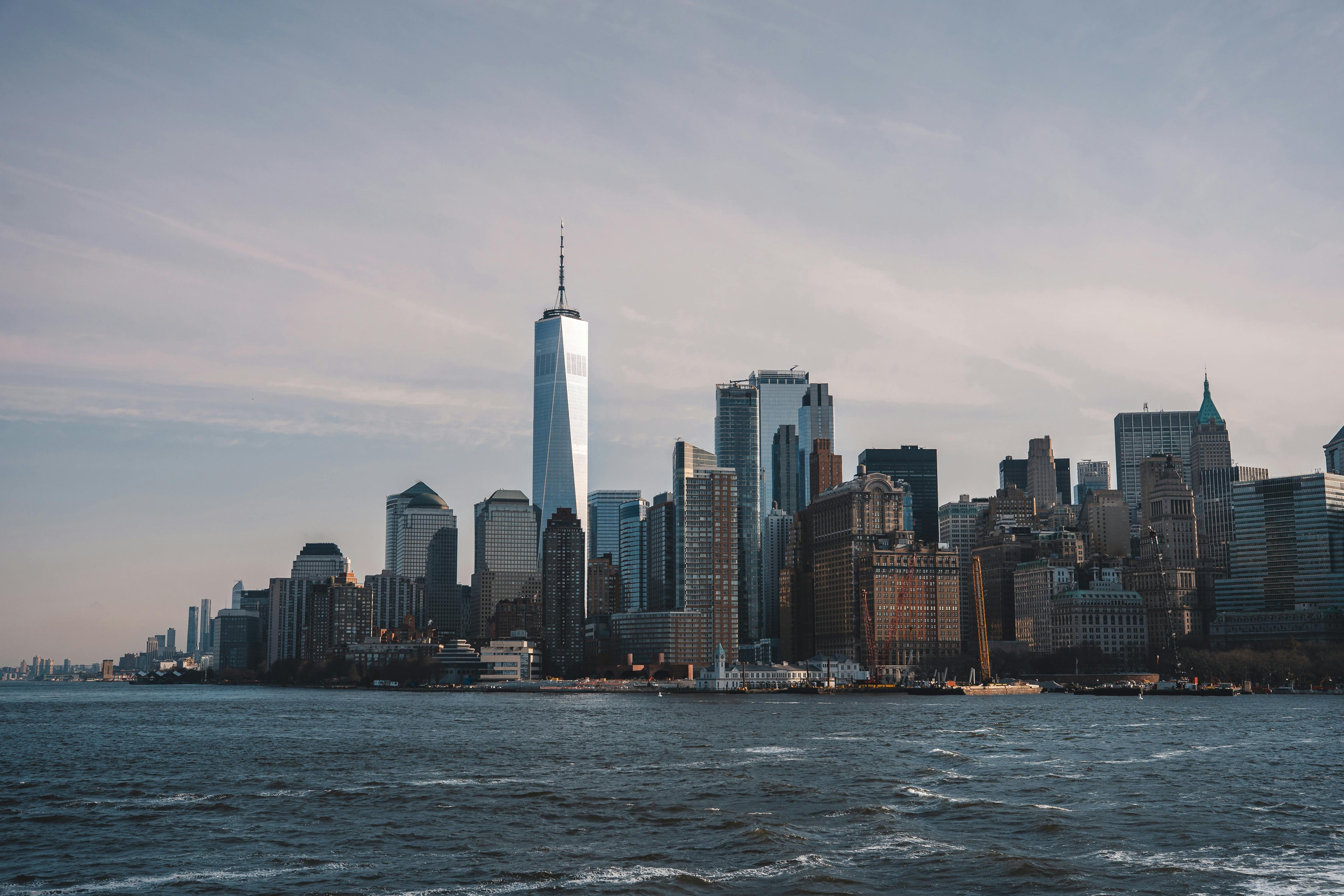 New York skyline with water view with sun low in sky. Photo by Willian Justen de Vasconcellos: https://www.pexels.com/photo/new-york-city-skyline-featuring-one-world-trade-center-32922191/